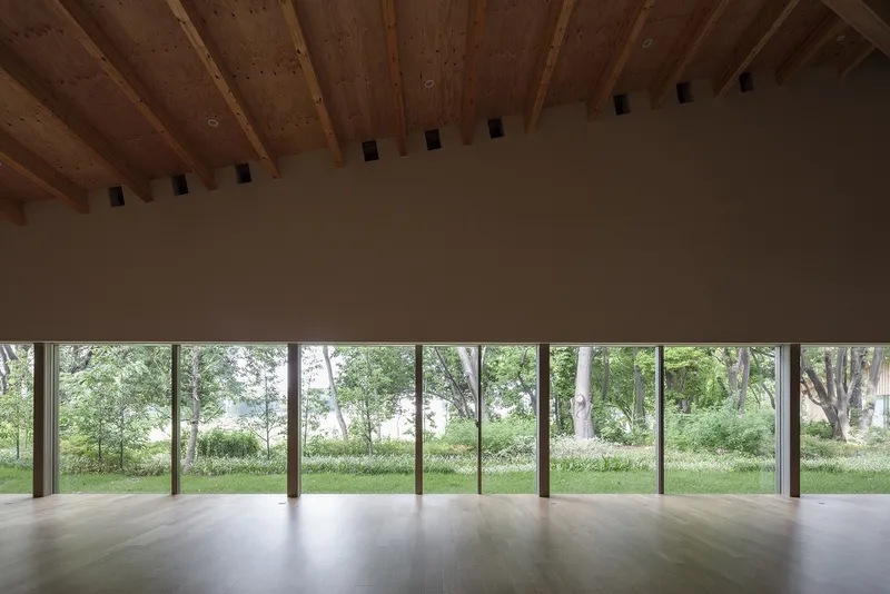 Glass wall spanning the length of an interior space overlooking a green lawn with mature trees