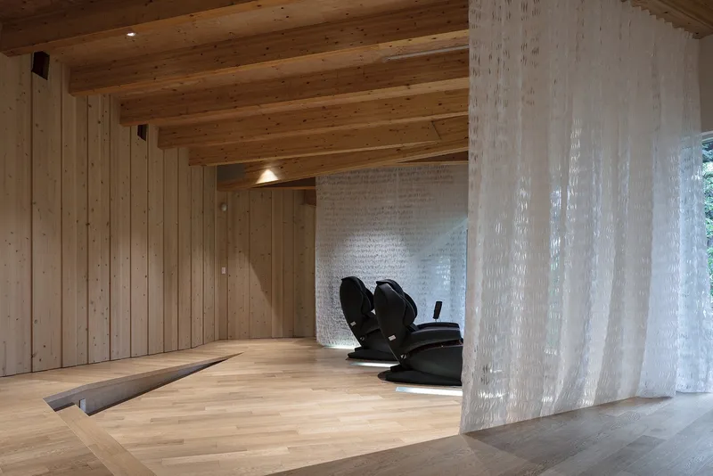 Interior corner with translucent corrugated partition and timber ceiling beams above wood flooring