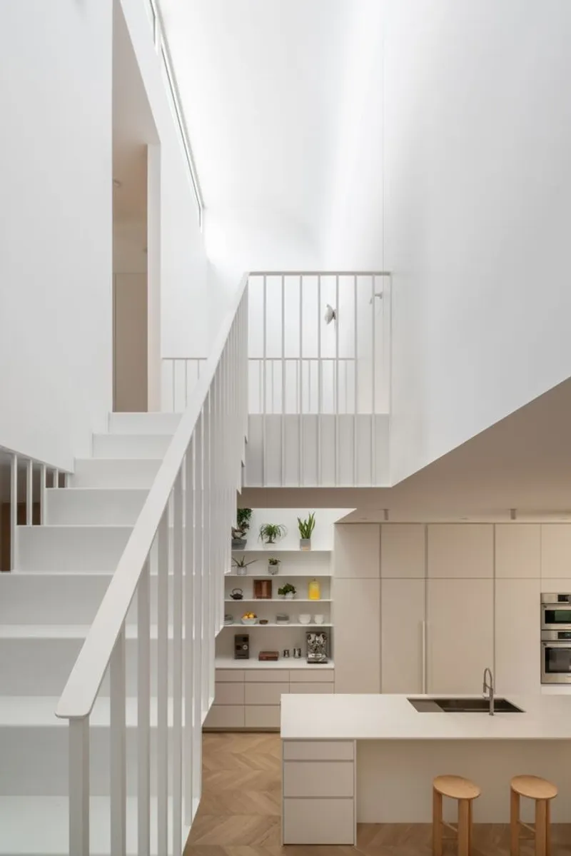 White-painted staircase with vertical balusters rising past the kitchen island and open shelving