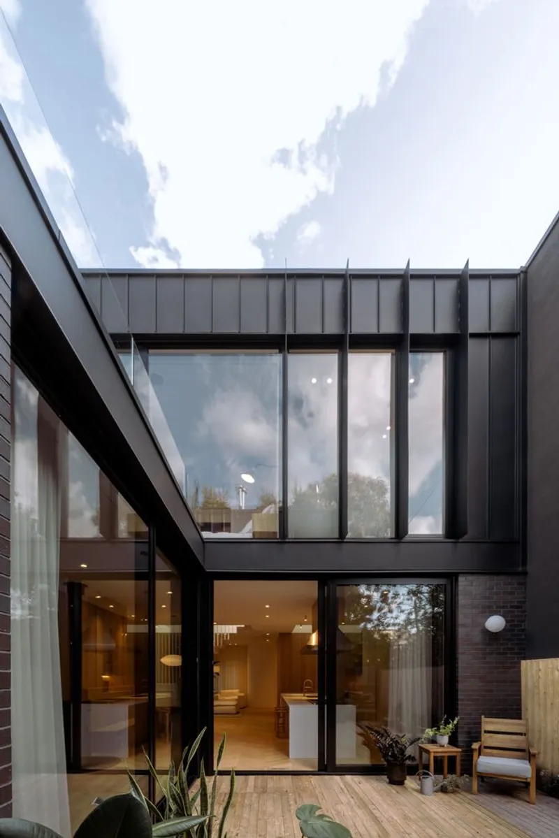 Courtyard view of the black metal facade with full-height glazing beneath a cloudy afternoon sky