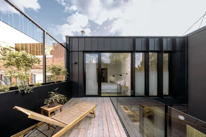 Timber deck terrace with planted beds and lounge chair facing the dark metal and glass rear elevation