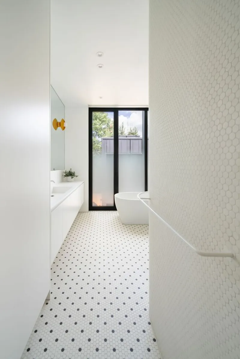 Bathroom with white hexagonal tile wall, terrazzo floor and black-framed glazed door to garden