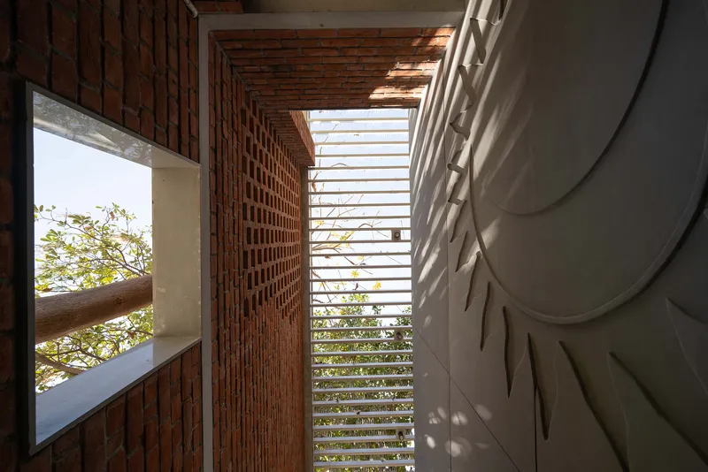 Interior corridor with perforated brick wall and horizontal louver screen framing greenery beyond
