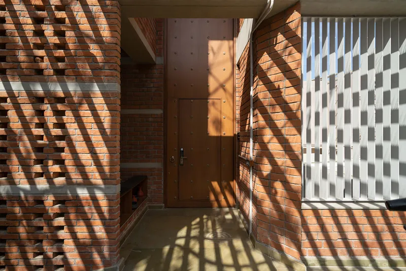 Entry vestibule with metal door and diagonal shadow patterns cast across brick and white screen walls