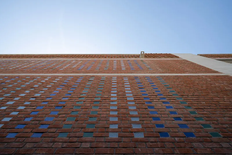 Upward view of brick facade with scattered blue tile accents under clear sky