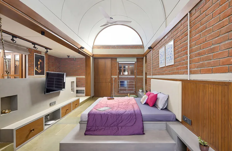 Bedroom with vaulted ceiling, exposed brick walls, timber paneling, and arched skylight overhead