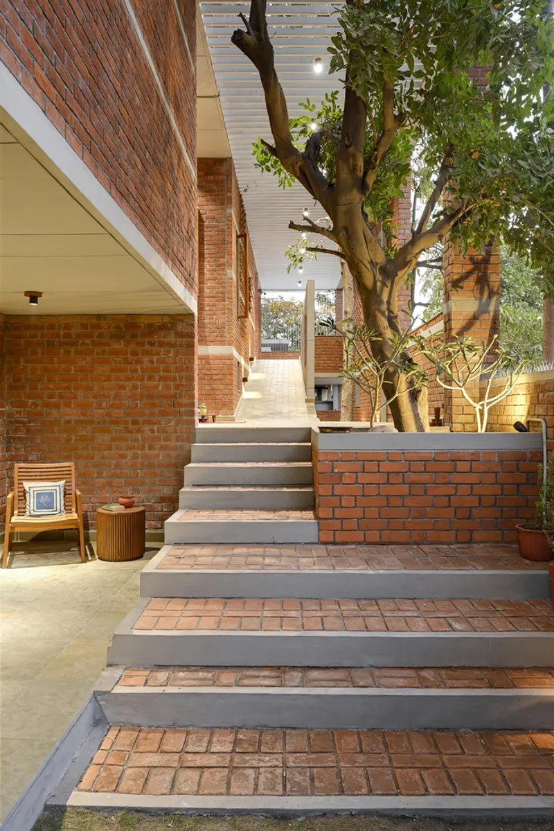 Outdoor staircase with brick treads and concrete risers ascending past a preserved tree in the courtyard