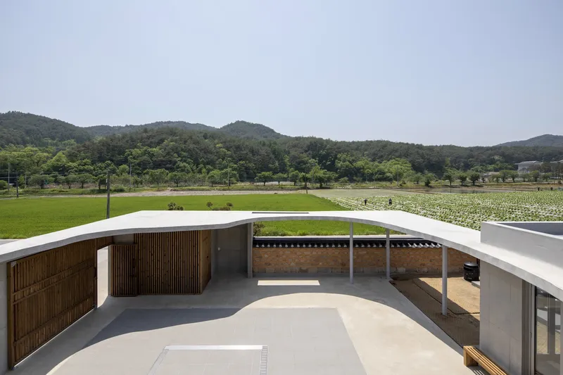 Curved courtyard terrace overlooking rice paddies and forested hills under overcast skies