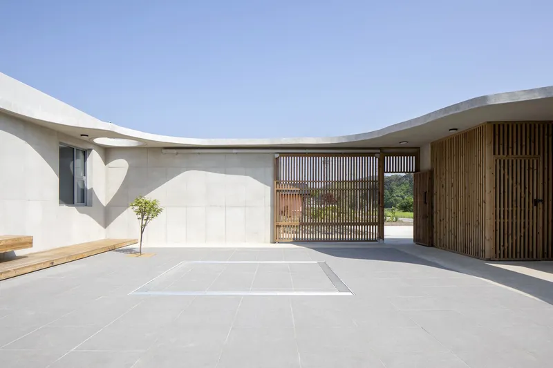 Courtyard with vertical timber gate panels casting heart-shaped shadow on concrete wall in sunlight