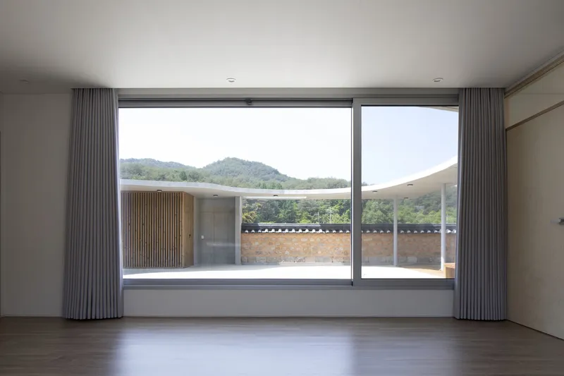 Interior room with full-height glazing and grey curtains framing view of distant hills