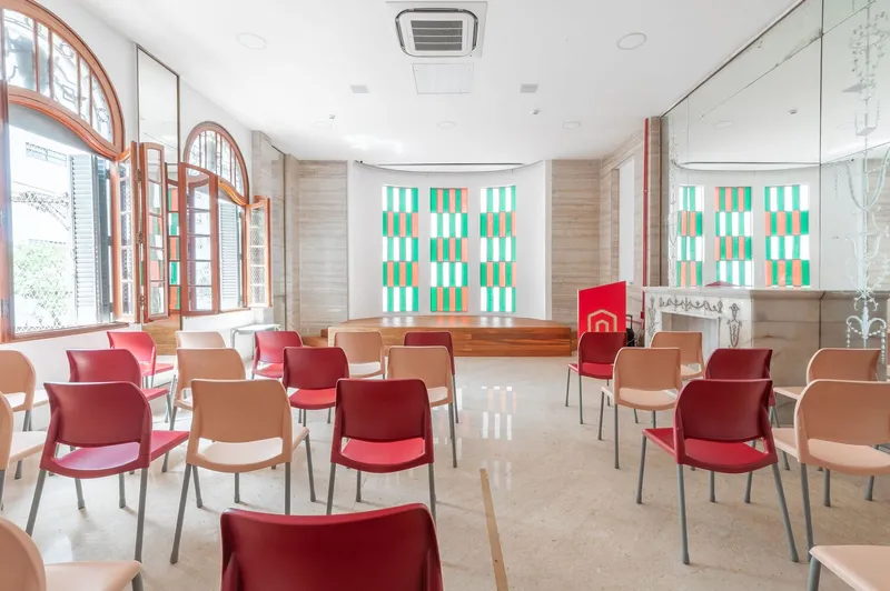Meeting room with arched timber windows and rows of red and tan chairs facing a checkered tile backdrop