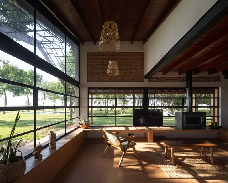 Double-height living space with exposed timber ceiling beams and sunlight filtering through steel-framed windows