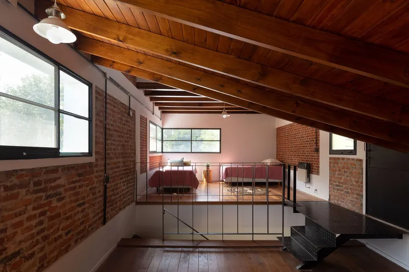 Mezzanine bedroom with exposed brick walls and steel railing under sloped timber ceiling