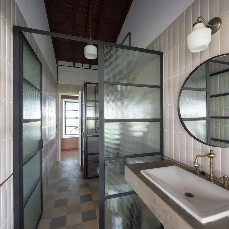 Bathroom with vertical white tile walls and textured glass shower partition in steel frame