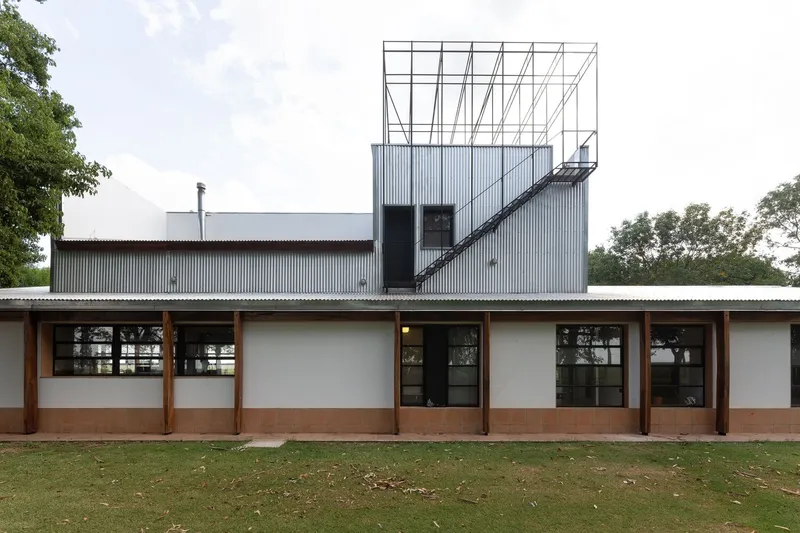 Rear elevation with timber-framed glazing bays beneath a corrugated metal roof and open steel framework tower