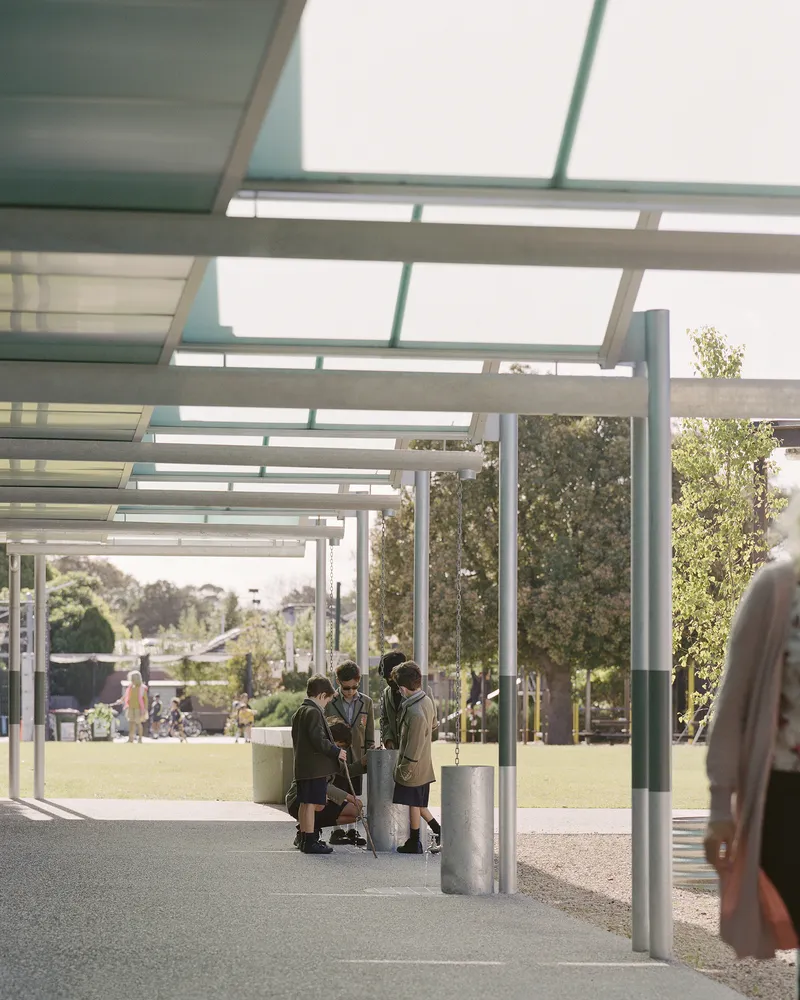 Covered walkway with steel beams and glazed roof panels sheltering children in school uniforms