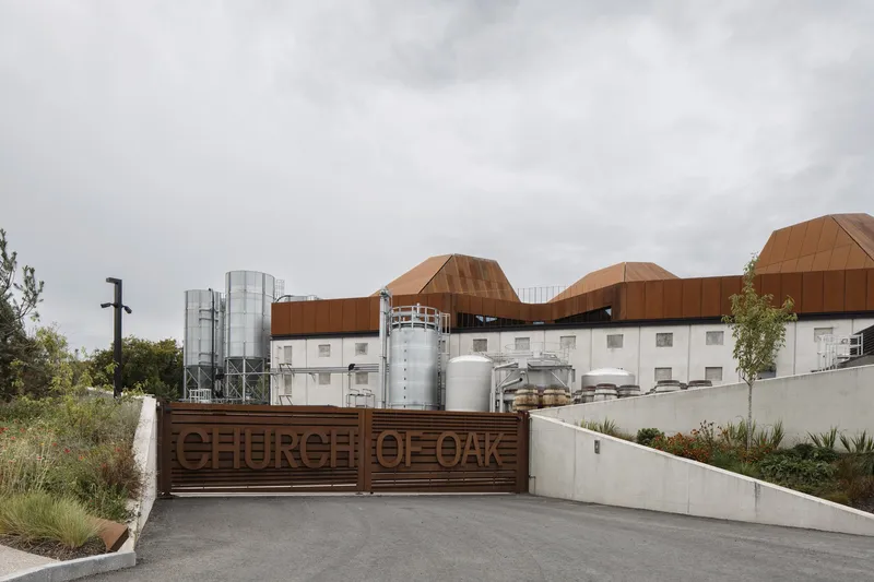 Entry gate with timber cladding and concrete walls leading to the complex under overcast skies