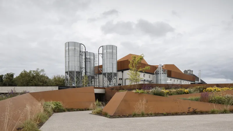 Weathered steel landscape walls and planted beds frame the approach to the industrial silos and roof forms