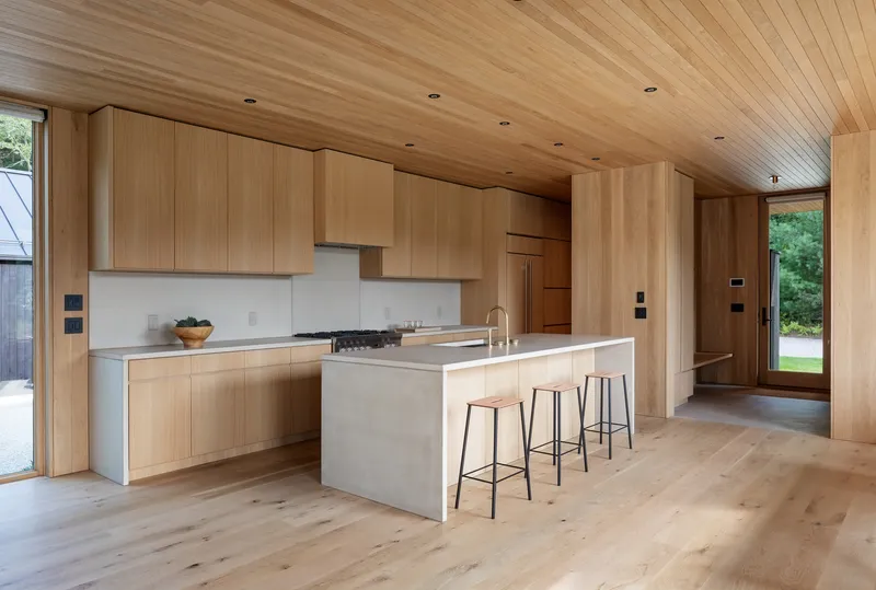 Open kitchen with light wood cabinetry, white quartz island, and tongue-and-groove ceiling under natural light