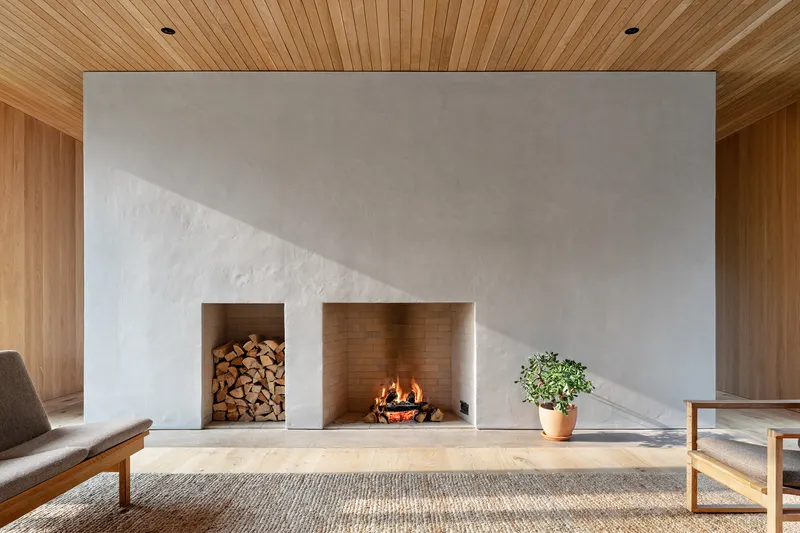 White plaster fireplace wall with timber-lined hearth and firewood storage alcove beneath a tongue-and-groove ceiling