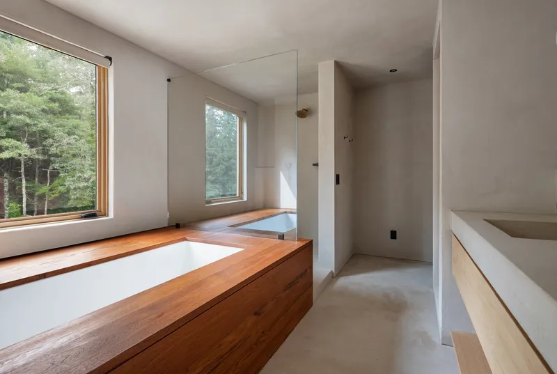 Bathroom with timber-clad soaking tub beneath a deep window sill and white plaster walls