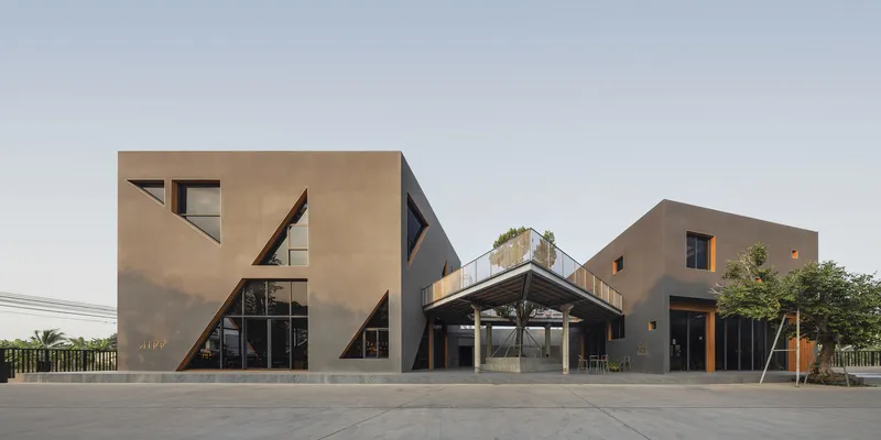 Street view of tan facade with angular window cutouts across multiple volumes under an overcast sky