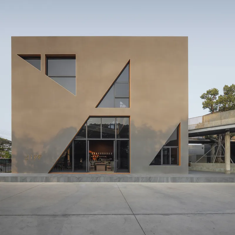 Facade detail showing triangular window openings cut into the tan plastered wall above a concrete base