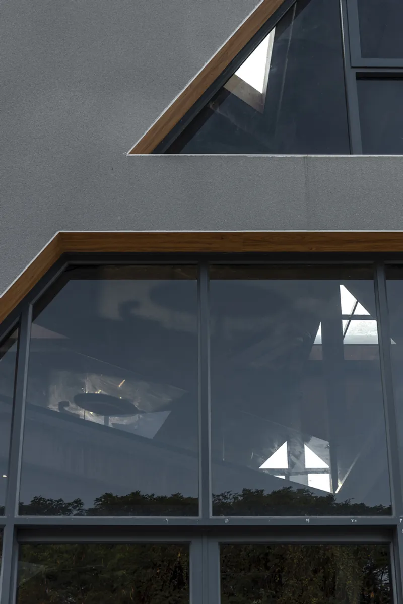 Facade detail showing timber-framed triangular windows in grey rendered walls with glass reflections