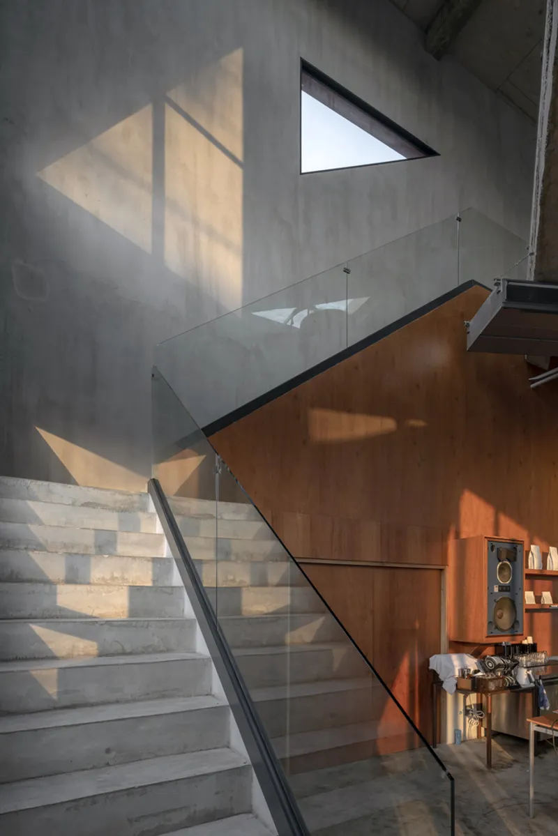Concrete staircase with glass guardrail beneath triangular skylights casting geometric shadows on the wall