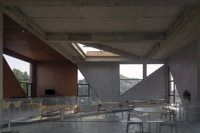 Open dining hall with board-formed concrete walls, triangular clerestory windows and scattered wooden tables