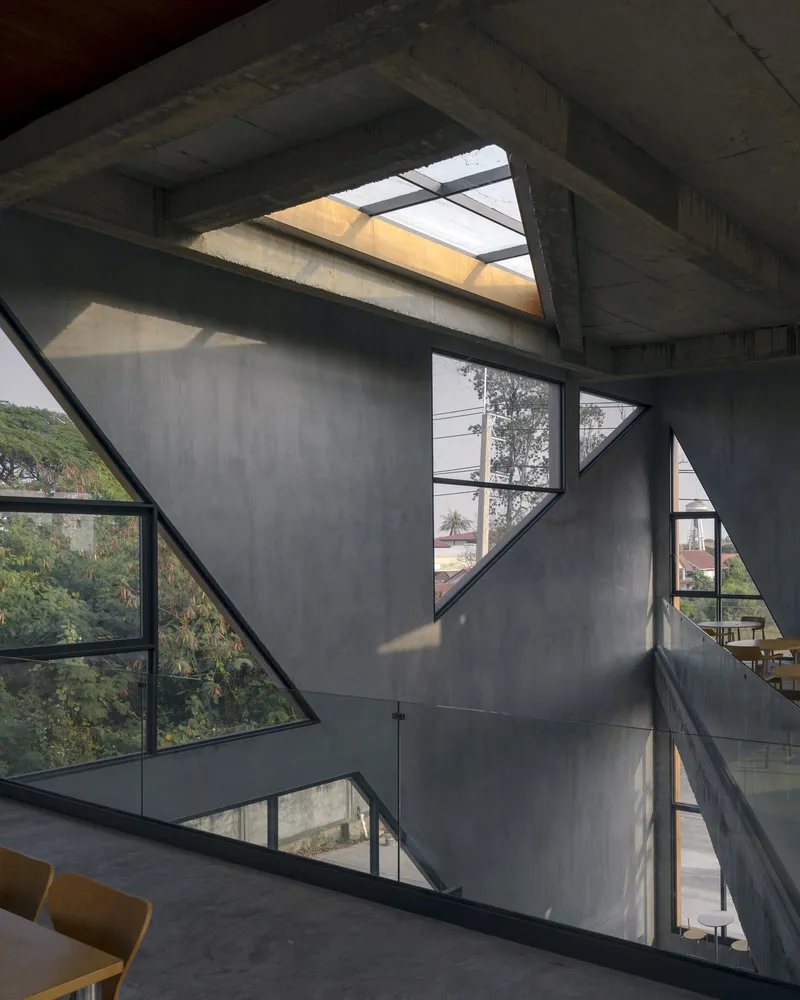 Triple-height atrium with angular concrete walls and triangular skylights casting geometric shadows
