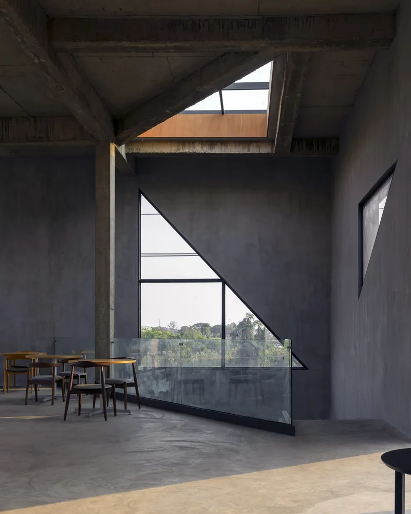 Dining area beneath concrete ceiling with triangular window overlooking trees and polished concrete floor
