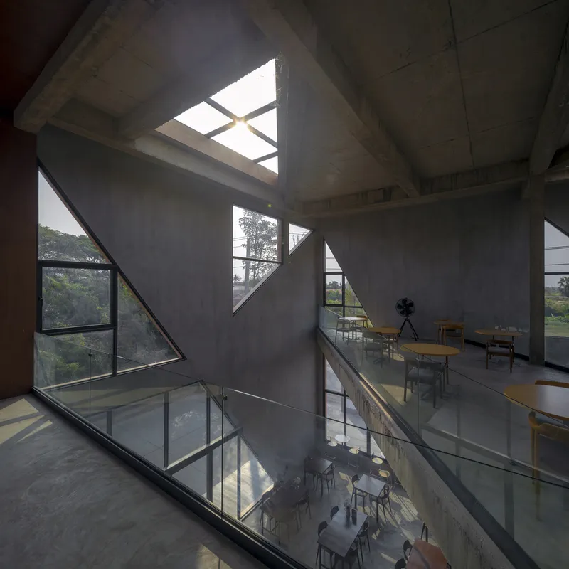 Double-height concrete interior with triangular skylights and windows casting geometric shadows across glass-railed mezzanines
