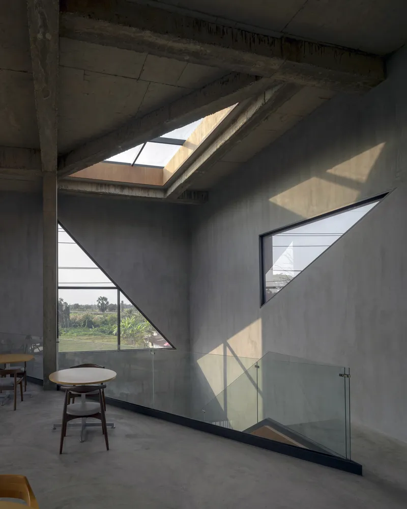 Triangular skylight above concrete wall with angled window openings projecting geometric shadows onto the floor