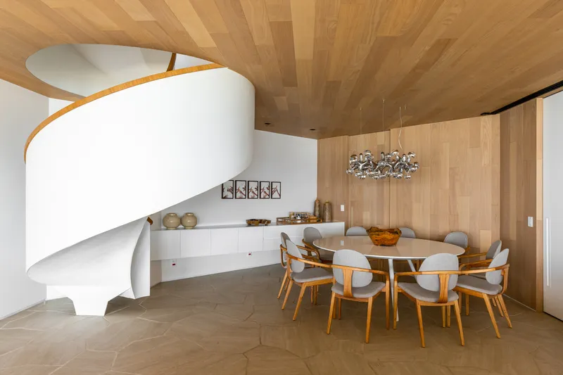 Dining area with sculptural white staircase and radiating timber ceiling panels