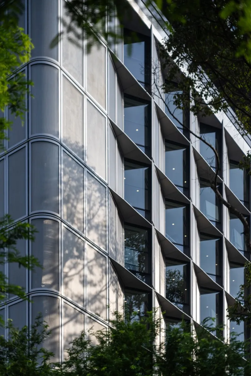 Angled facade with glass and concrete panels framed by curved balconies and dappled tree shadows
