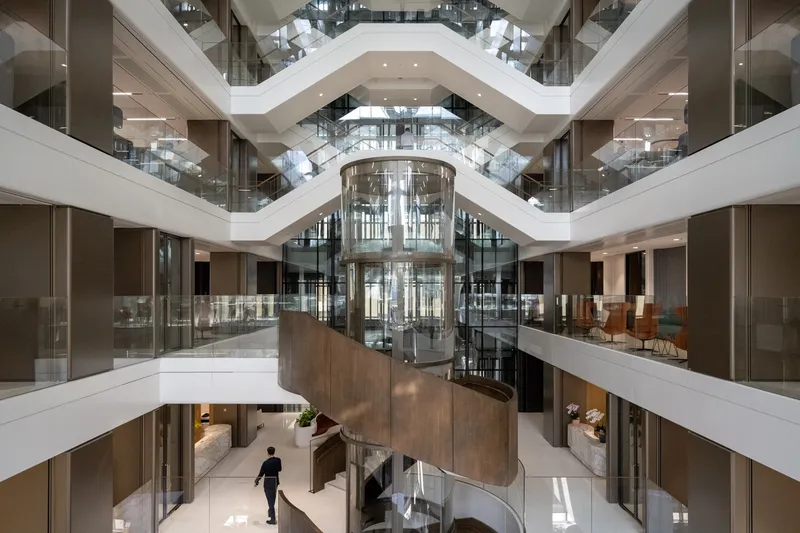 Multi-story atrium with stacked zigzag balconies surrounding a central cylindrical glass elevator shaft
