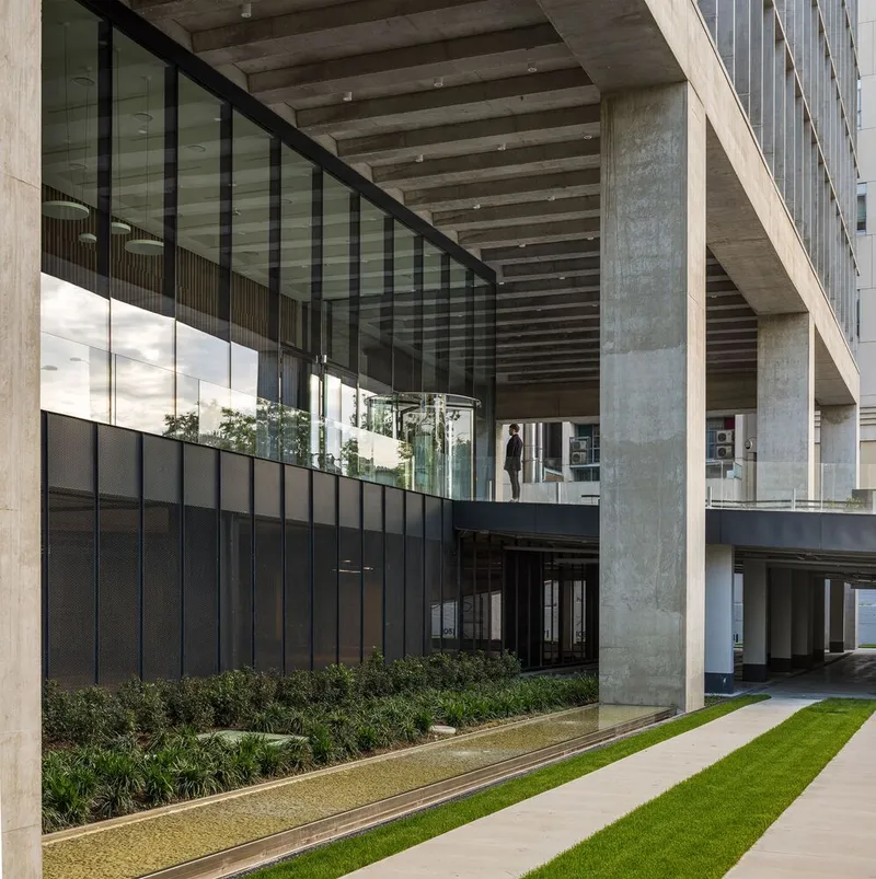 Ground-level courtyard with planted beds below concrete beams and black metal-clad upper volume