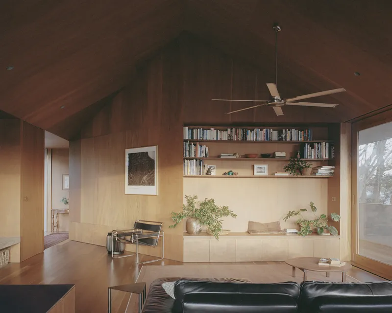 Living room with plywood-lined vaulted ceiling and built-in shelving beneath a pendant ceiling fan