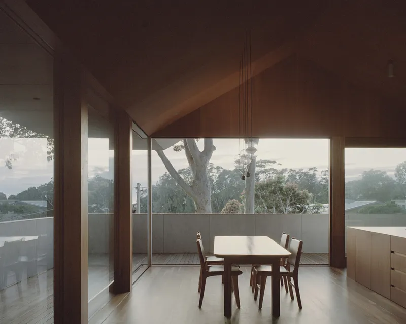 Dining area framed by timber columns opening to a terrace with eucalyptus trees in morning mist