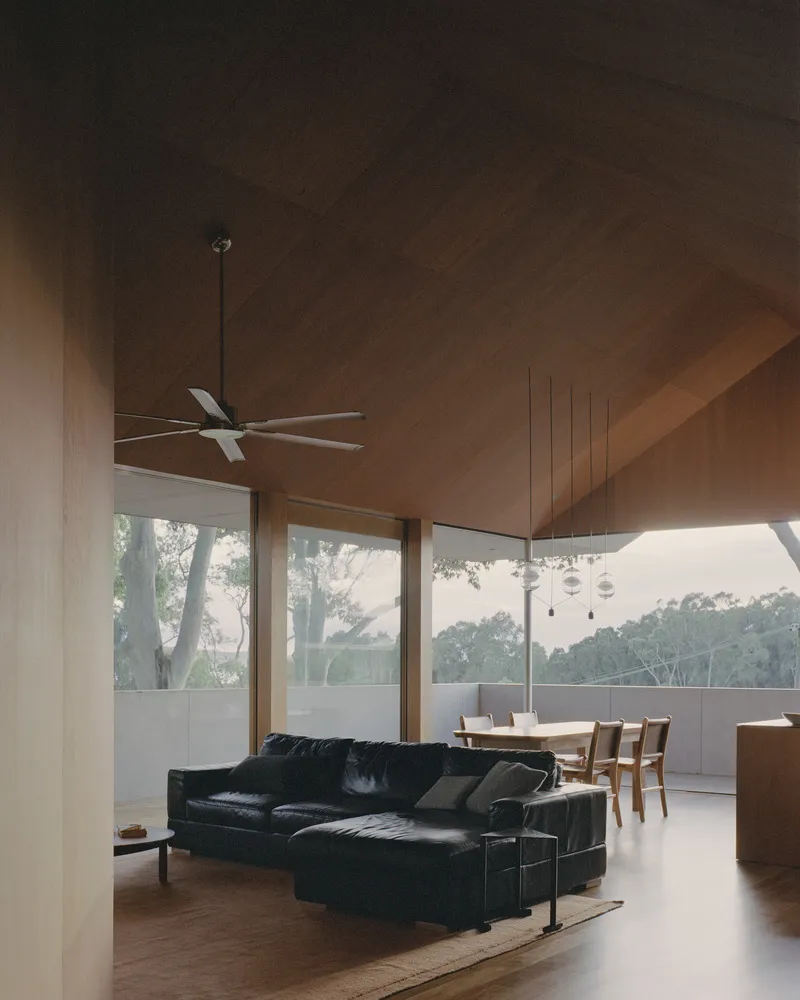 Open-plan living space with plywood-paneled cathedral ceiling and clerestory glazing at dusk