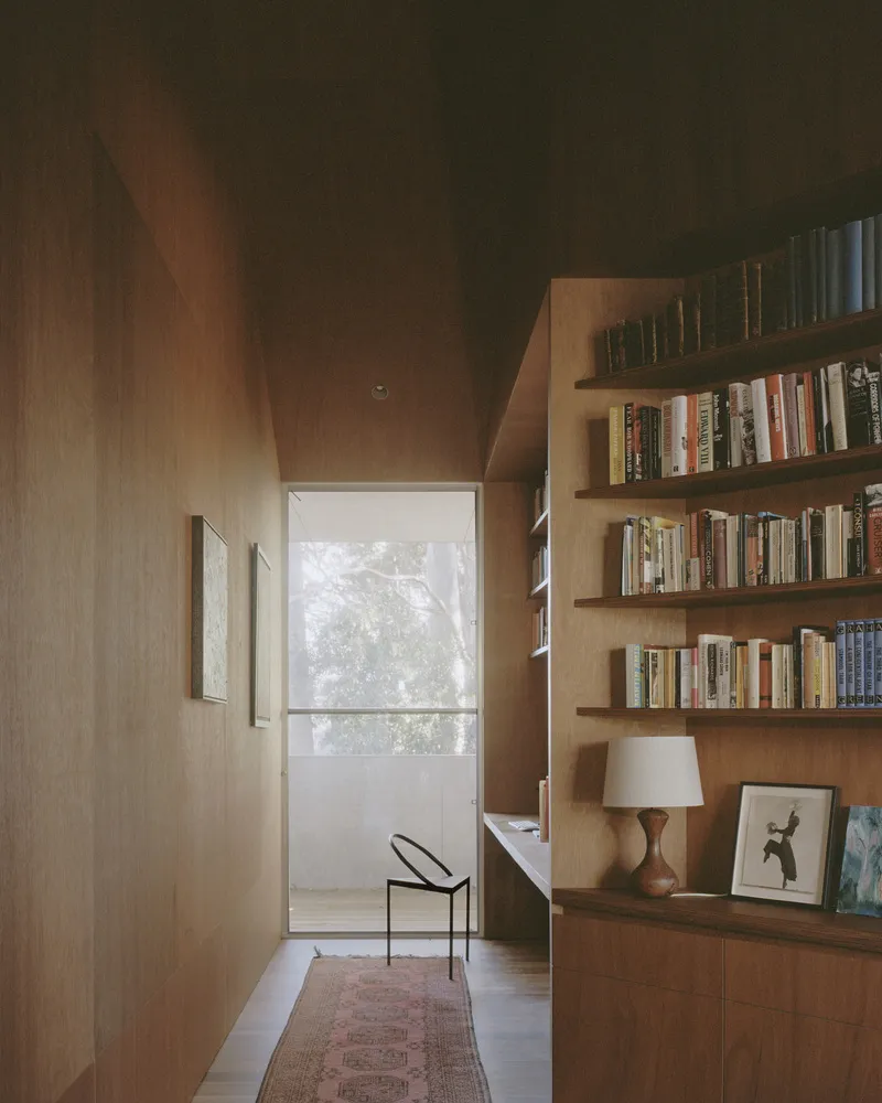 Timber-lined hallway with built-in bookshelves leading to a glazed door framing trees outside