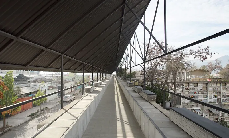 Covered seating area with concrete benches and steel truss canopy overlooking a cemetery wall and bare trees