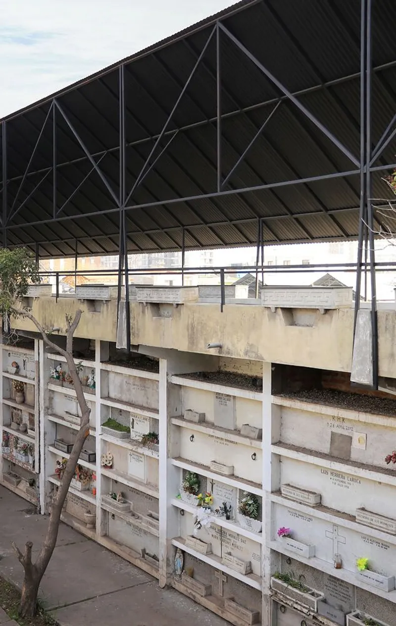 Steel truss canopy over terraced concrete seating facing weathered columbarium niches with memorial plaques