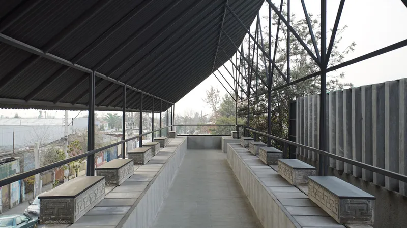 Linear seating terrace with concrete benches under a corrugated metal roof and exposed steel trusses