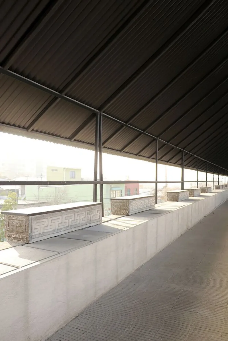 Concrete memorial benches with decorative carved panels beneath a corrugated canopy in diffused daylight