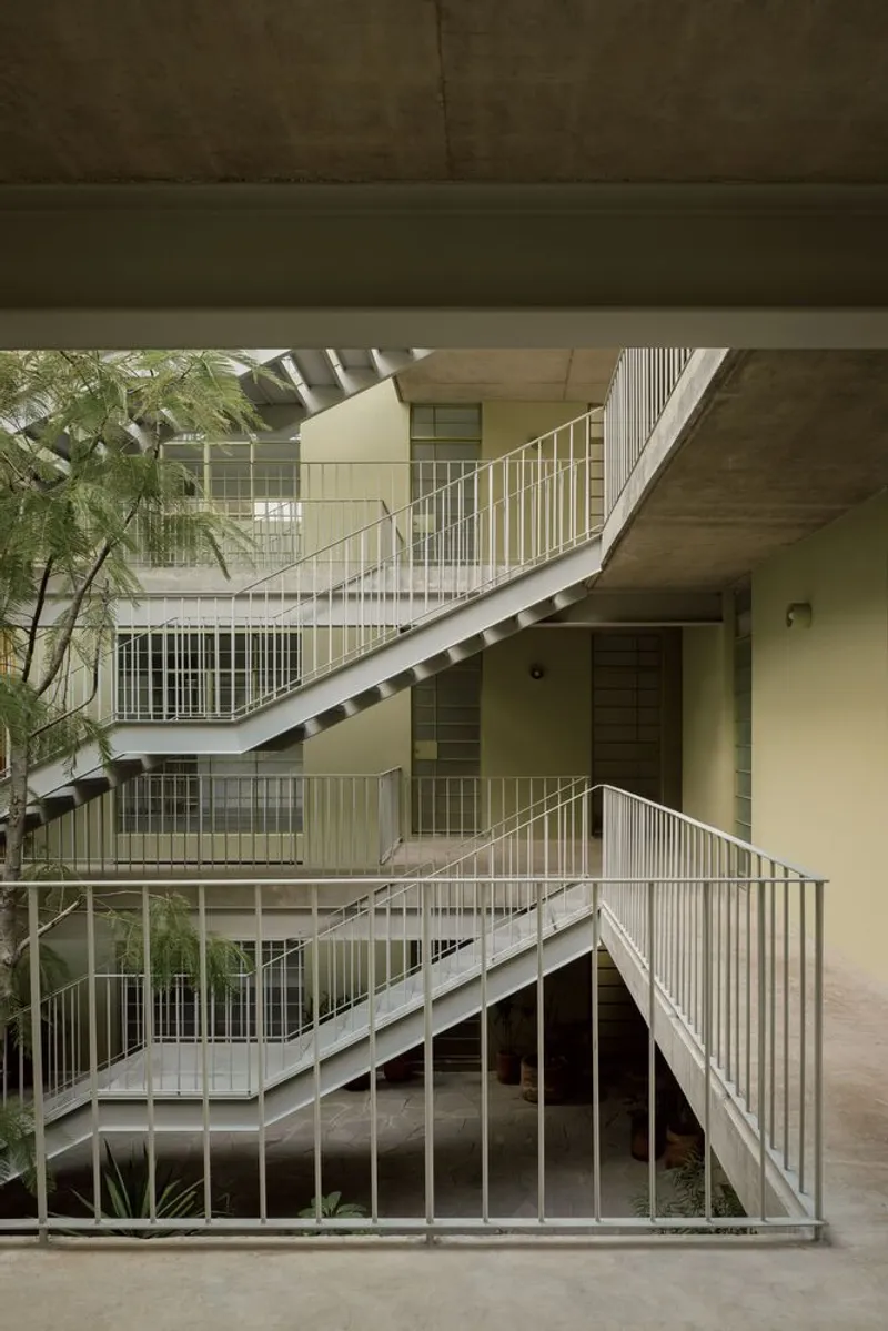 Zigzagging exterior staircases with metal railings ascending alongside a planted courtyard with trees