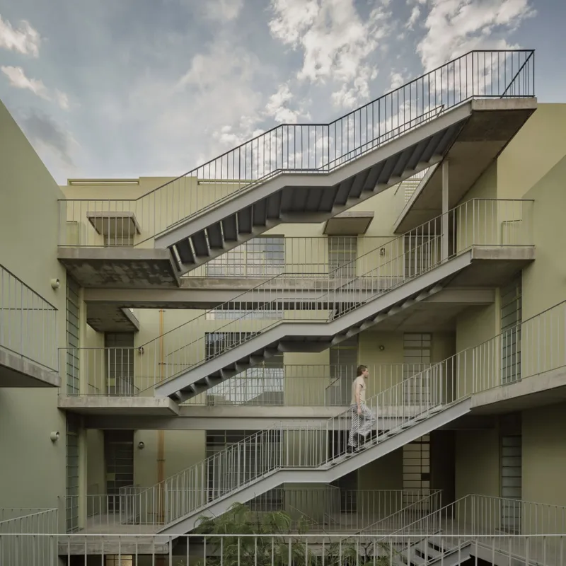 Exposed concrete staircases crisscrossing the courtyard facade with a figure on the upper landing under clouds