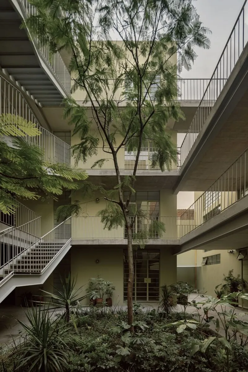 Internal courtyard with a tall tree rising through planted beds and metal stair balconies under overcast sky