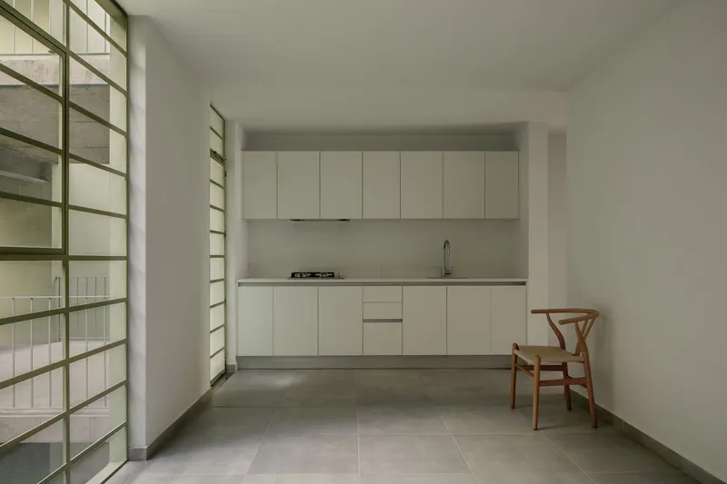Minimal kitchen with white cabinets and glass block window next to a single wooden chair on polished floor